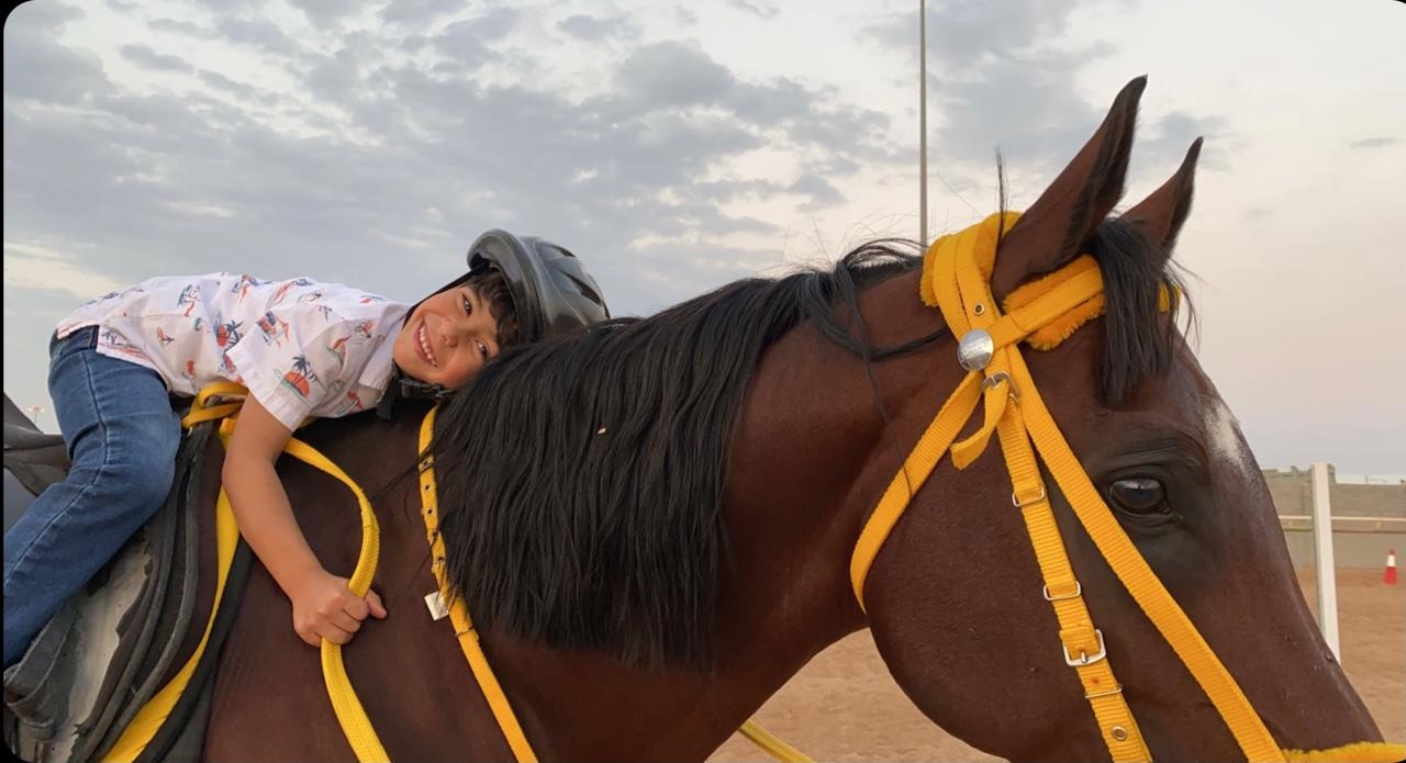 طفل بخوذة ركوب يميل بحنان على حصانه في البراق